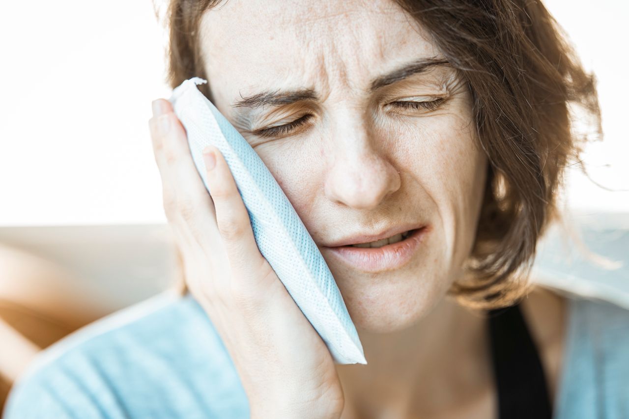 Masseter Neuromodulator Treatment for Bruxism 1 A woman in discomfort applying a cold compress to her cheek for relief from toothache pain.
